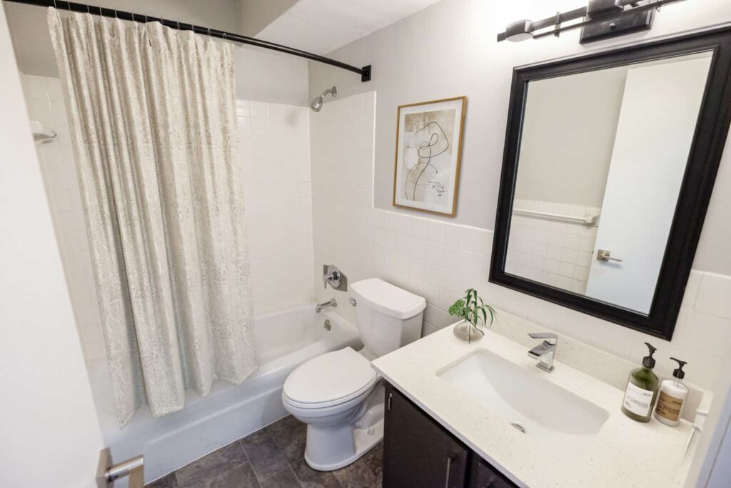 A bathroom with a full tub and shower and white, square tiles surround the walls.