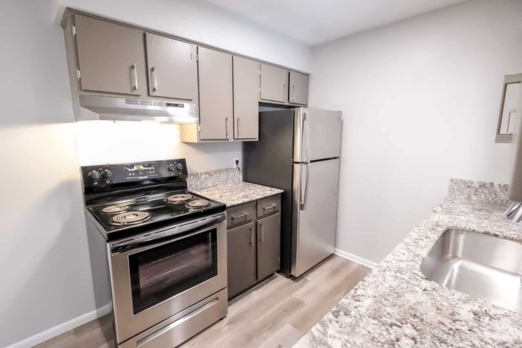 A kitchen with a dishwasher, farm-house sink, full range, and stainless-steel fridge.