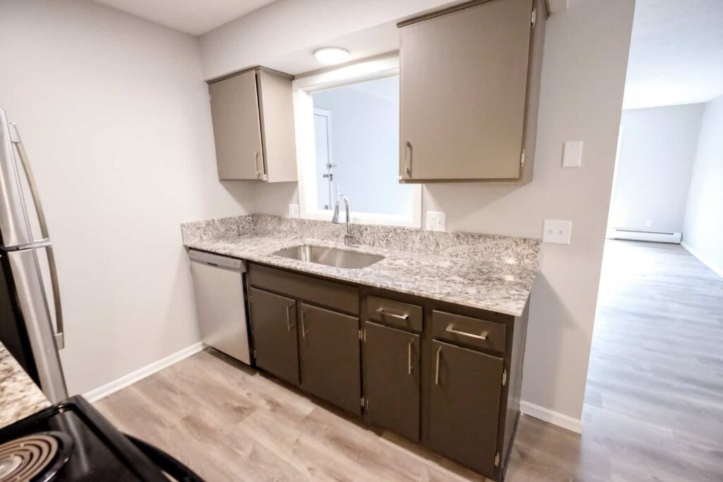 A kitchen with a dishwasher and farm-house sink with views from the sink into the living room.