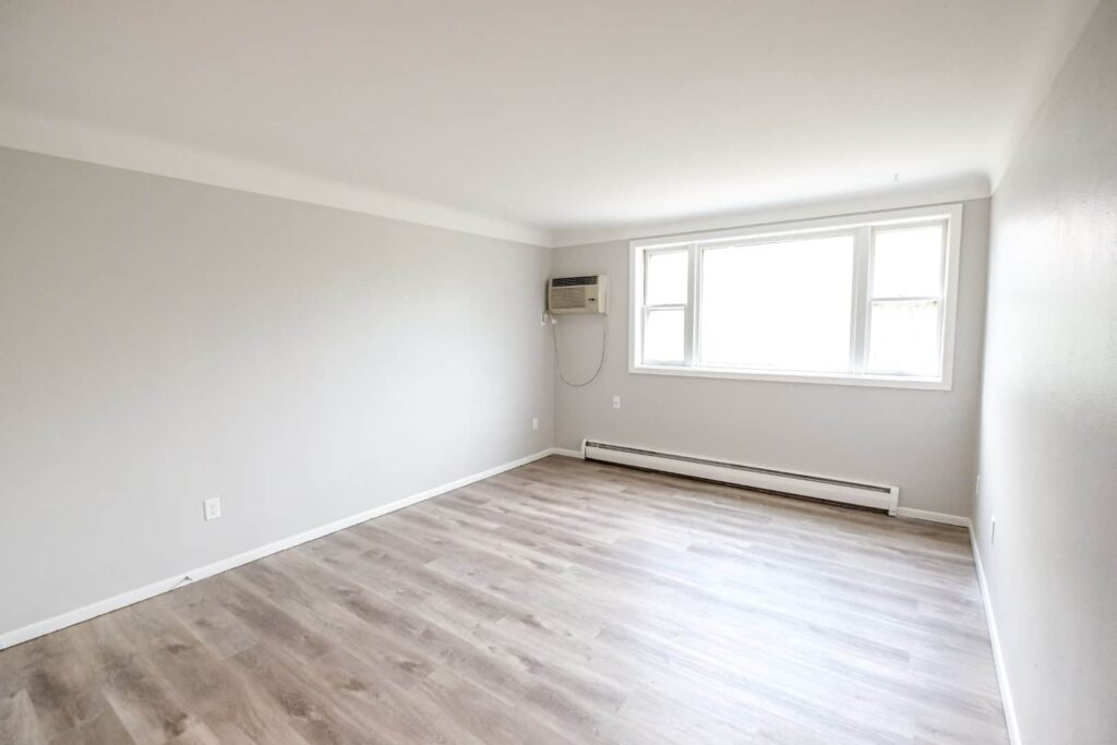 A bedroom with large windows allowing ample natural light and wood floors.
