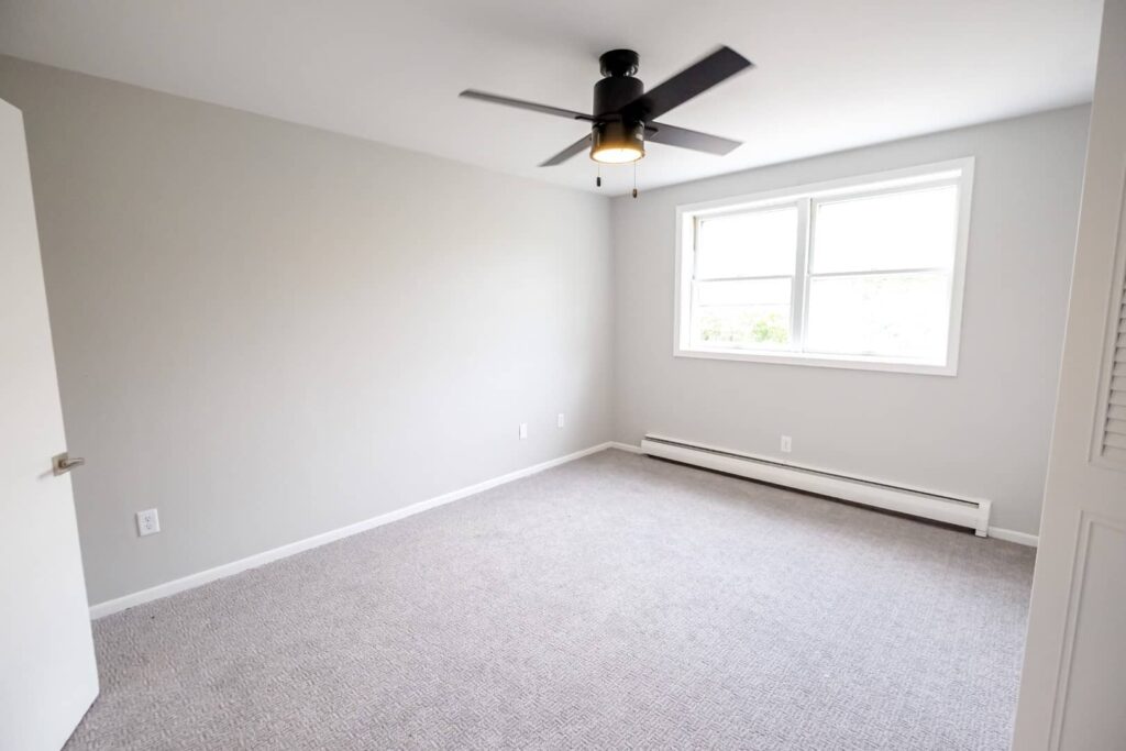 A bedroom with light pouring through the window and a modern ceiling fan.